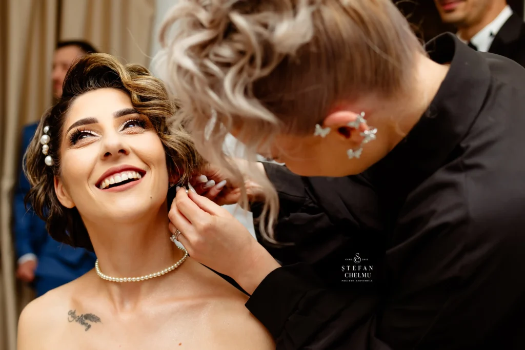 Detaliu mireasă zâmbind în timp ce îi sunt fixați cerceii, focus pe strălucirea ochilor, experiență Prețuim Amintirile®.